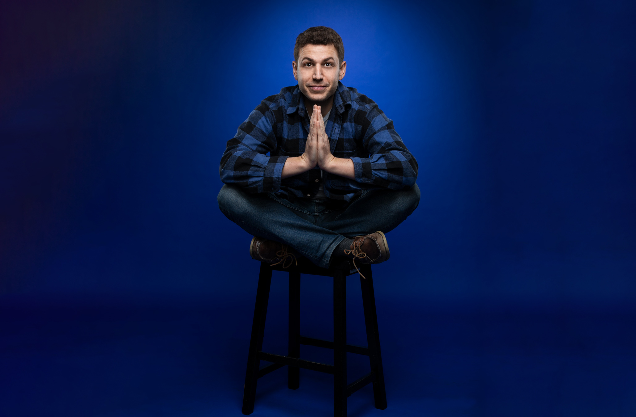 Ari Mannis seated cross-legged in his blue plaid shirt